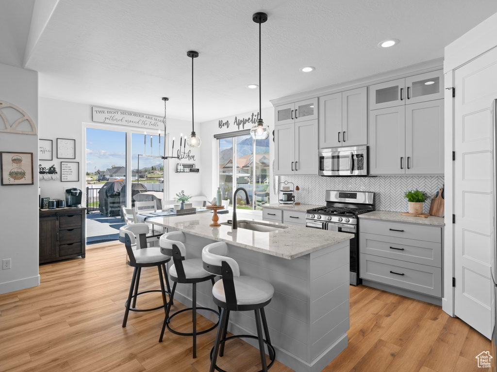 Kitchen featuring appliances with stainless steel finishes, a sink, an island with sink, light wood-style flooring, and recessed lighting