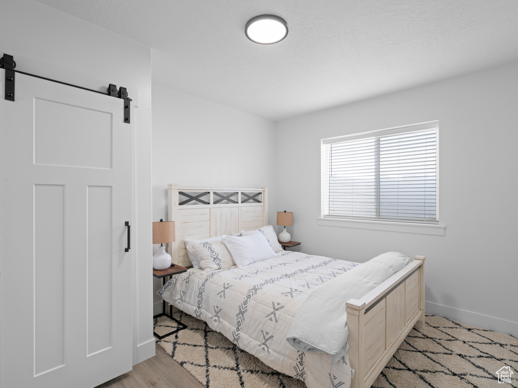 Bedroom featuring a barn door, baseboards, and light wood-style flooring
