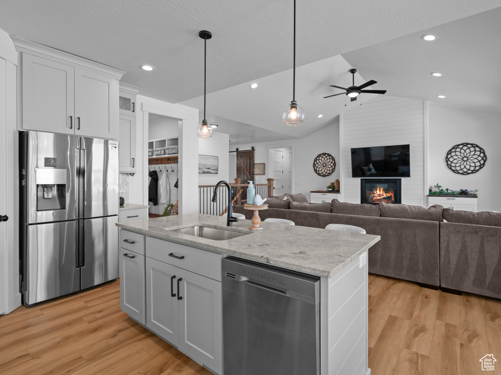 Kitchen featuring appliances with stainless steel finishes, open floor plan, a sink, ceiling fan, and lofted ceiling