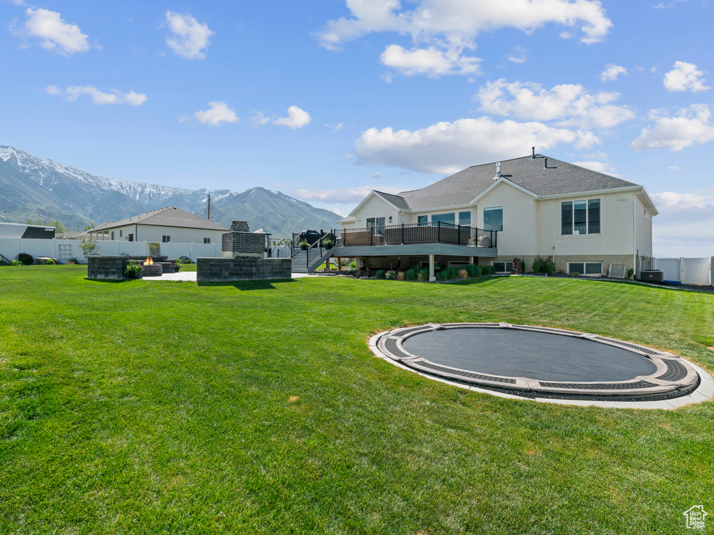 View of grassy yard featuring a trampoline, a deck with mountain view, and stairway