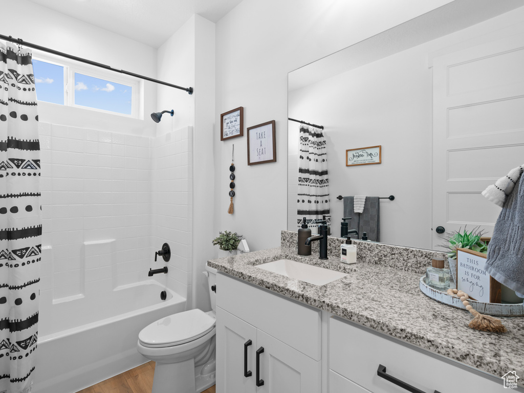 Bathroom with vanity, wood finished floors, toilet, and shower / tub combo