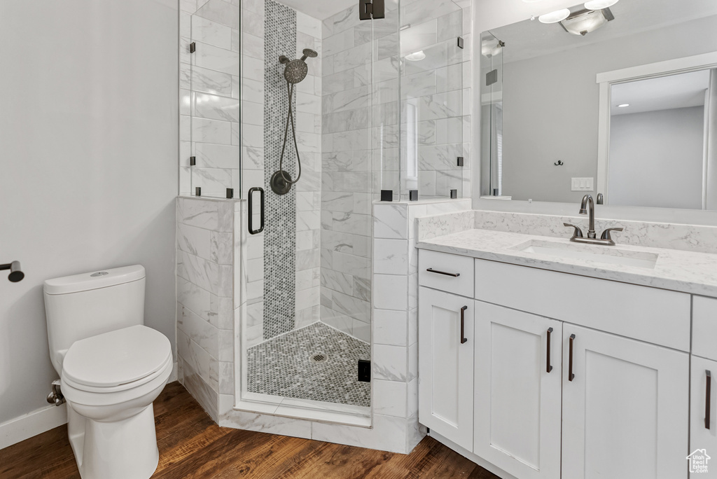 Full bathroom with vanity, toilet, a stall shower, baseboards, and wood finished floors