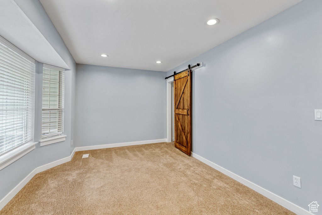 Spare room featuring recessed lighting, a barn door, light carpet, and baseboards