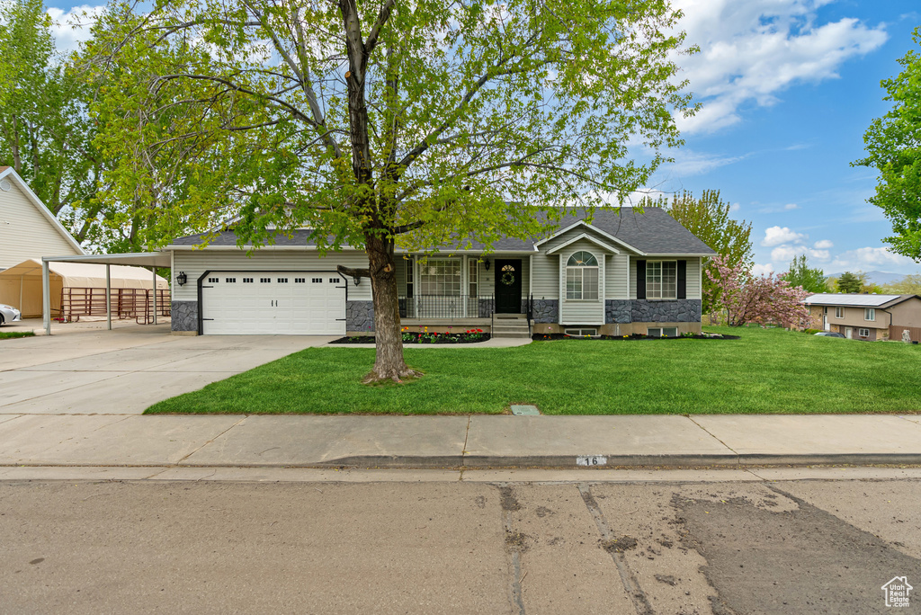 View of front of property with a front yard, covered porch, a carport, concrete driveway, and an attached garage