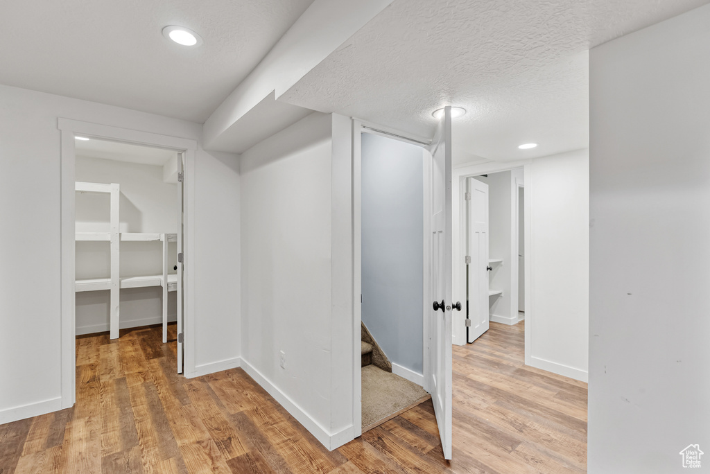 Finished below grade area with baseboards, light wood-type flooring, a textured ceiling, and recessed lighting