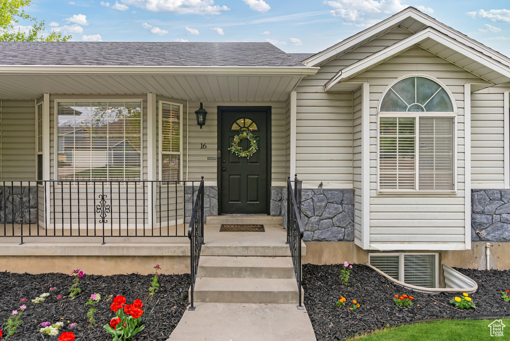 View of exterior entry featuring visible vents, a porch, a shingled roof, and stone siding