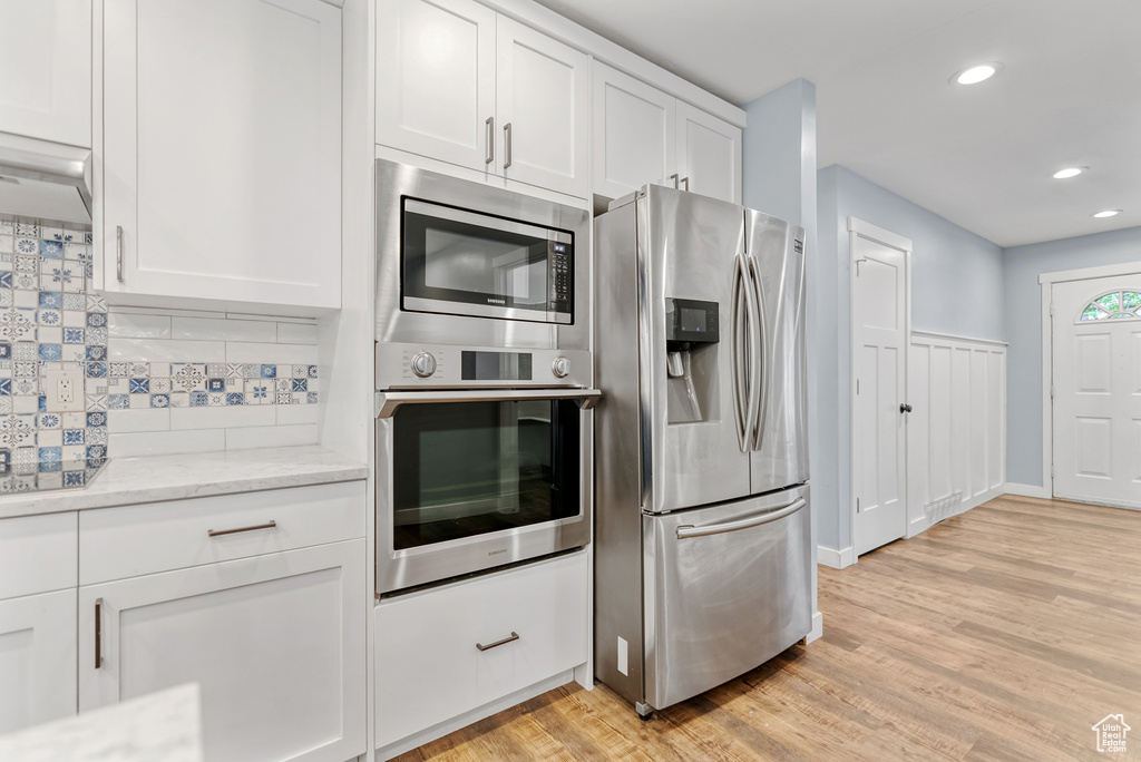 Kitchen featuring tasteful backsplash, recessed lighting, light wood-style floors, appliances with stainless steel finishes, and white cabinets