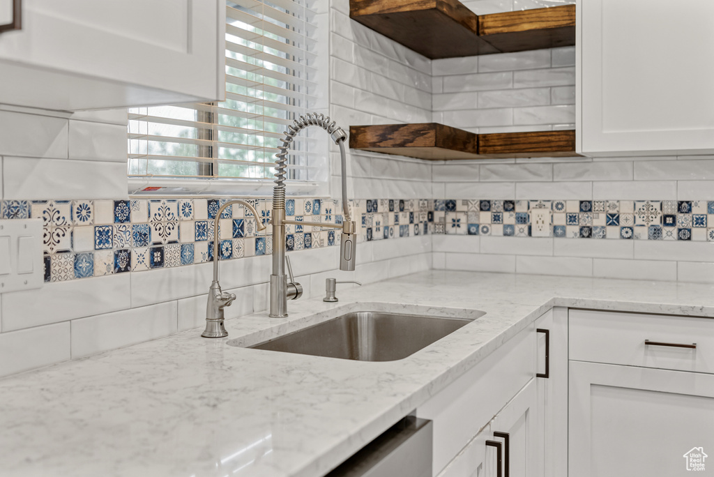 Kitchen with a sink, white cabinets, light stone counters, and decorative backsplash