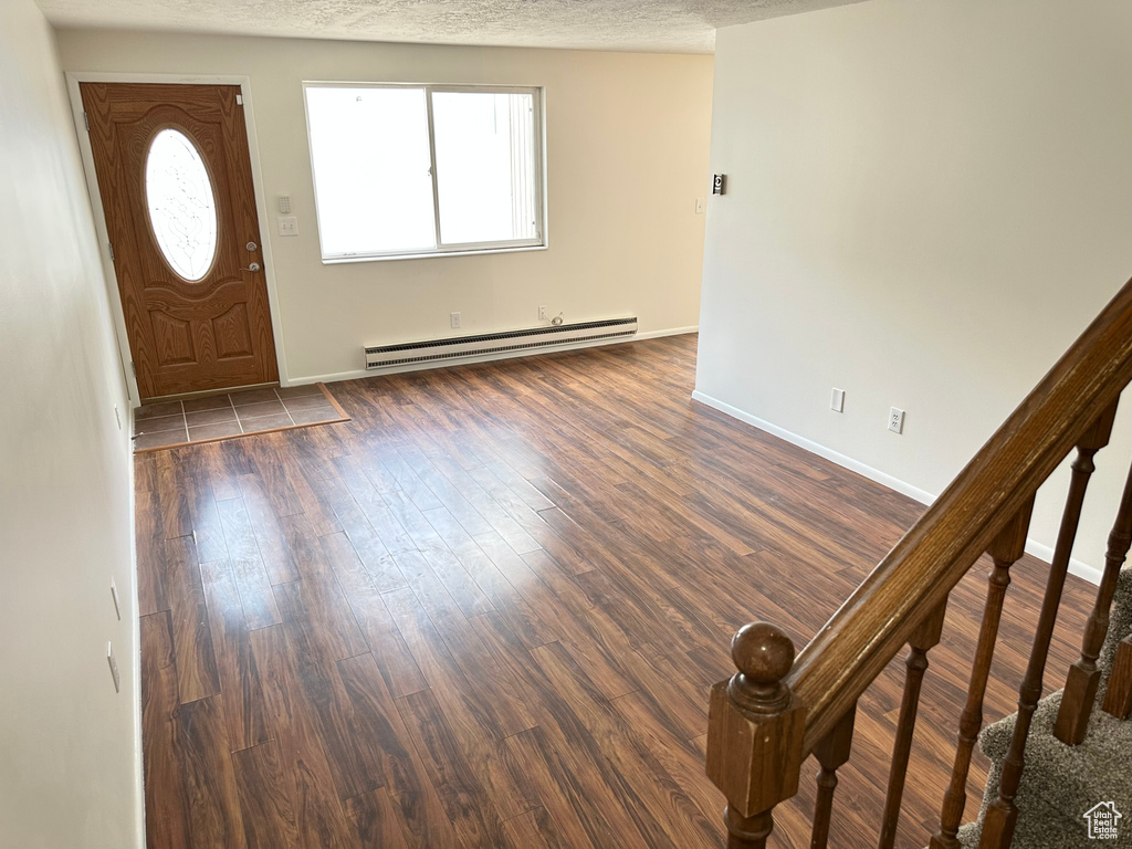 Entrance foyer with a baseboard radiator, stairway, dark wood-type flooring, baseboards, and a textured ceiling