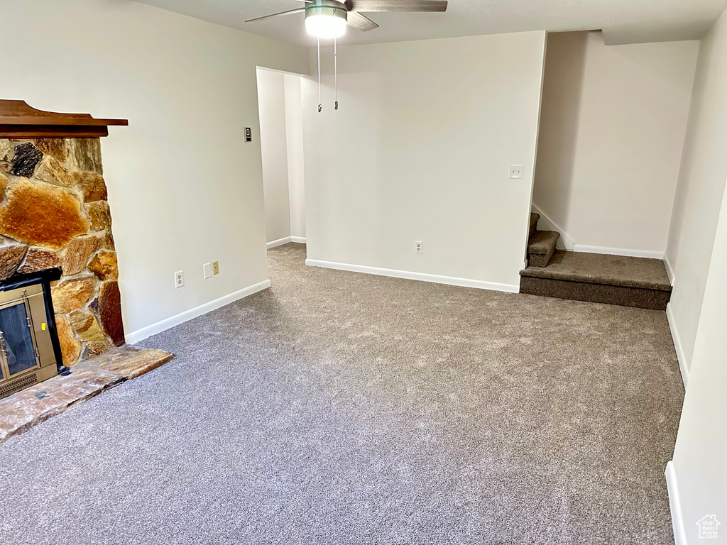 Unfurnished living room with ceiling fan, carpet, stairs, a stone fireplace, and baseboards
