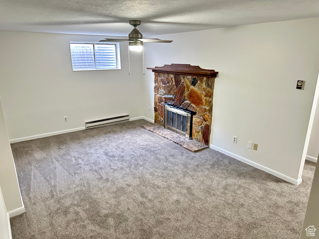 Unfurnished living room with a baseboard heating unit, ceiling fan, carpet flooring, a stone fireplace, and a textured ceiling