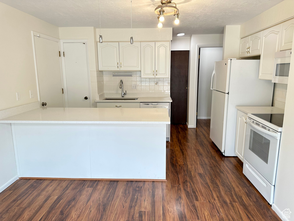 Kitchen featuring white appliances, a sink, a peninsula, white cabinetry, and dark wood-type flooring