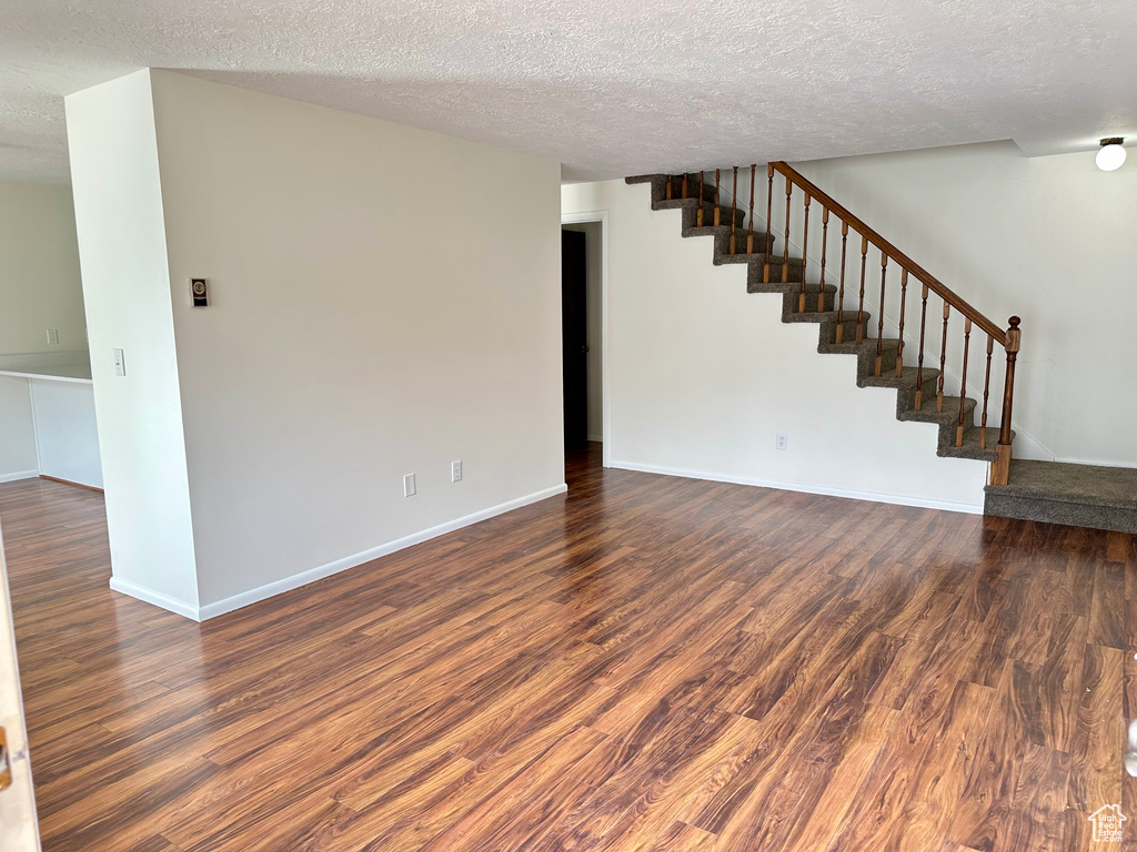 Unfurnished living room with stairway, a textured ceiling, wood finished floors, and baseboards