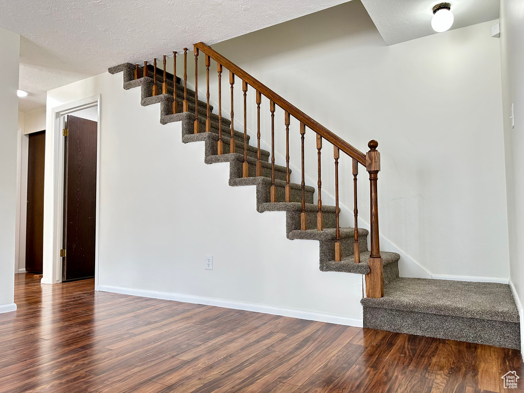 Stairs with wood finished floors, baseboards, and a textured ceiling