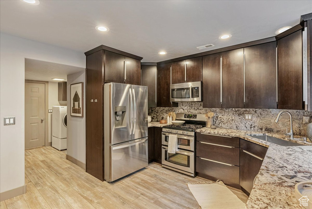 Kitchen with appliances with stainless steel finishes, washer / clothes dryer, a sink, dark brown cabinetry, and light wood finished floors