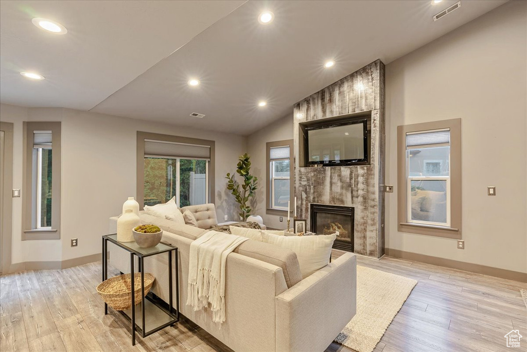Living room featuring a fireplace, light wood-style floors, vaulted ceiling, recessed lighting, and baseboards