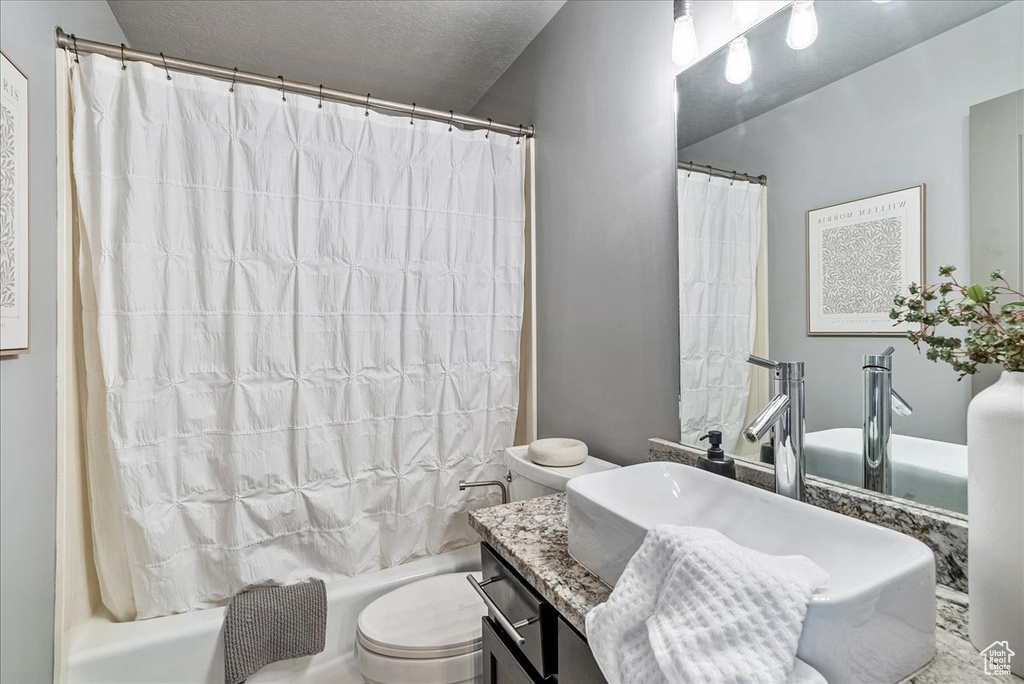 Full bathroom featuring toilet, shower / tub combo, vanity, and a textured ceiling