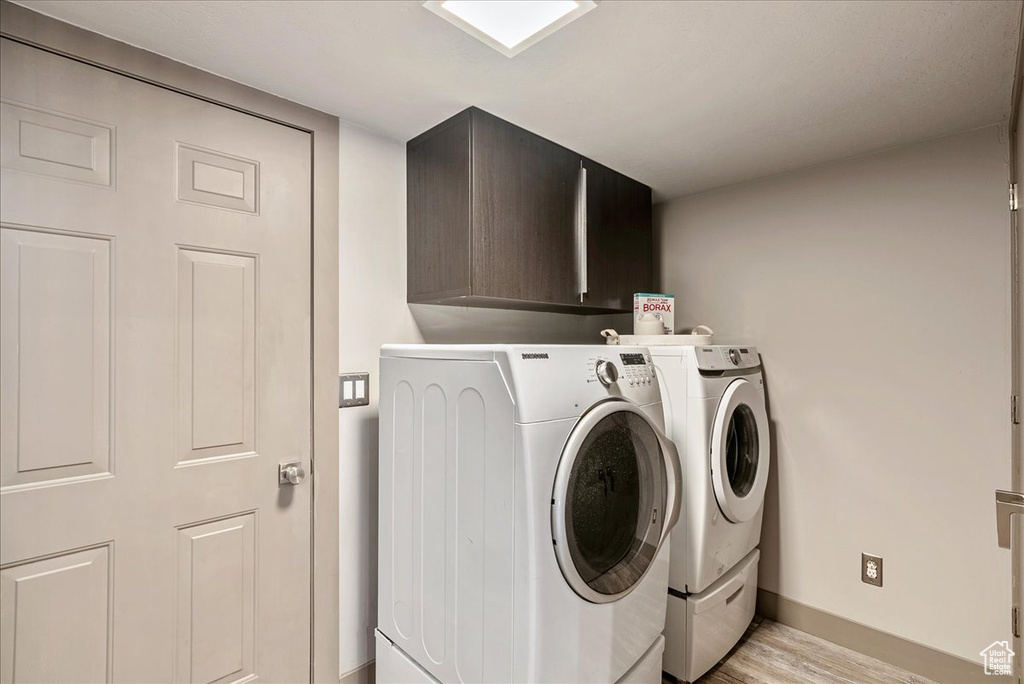 Washroom featuring washing machine and clothes dryer, cabinet space, baseboards, and light wood finished floors