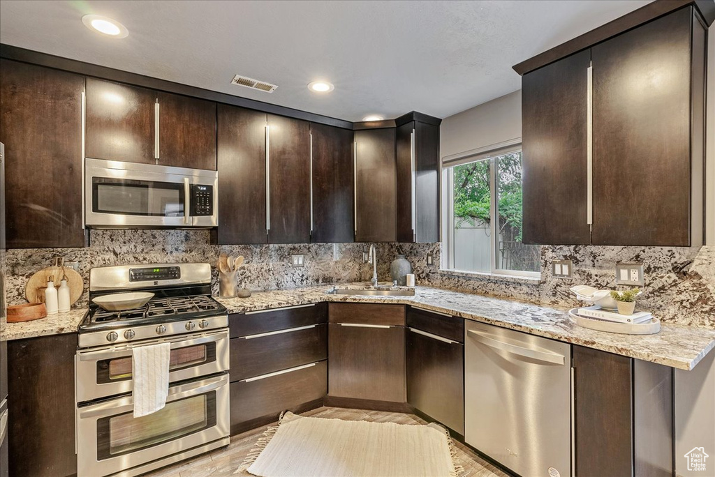 Kitchen featuring stainless steel appliances, a sink, dark brown cabinets, decorative backsplash, and recessed lighting