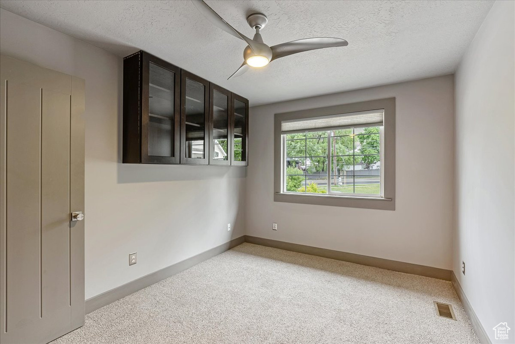 Carpeted spare room featuring ceiling fan, baseboards, and a textured ceiling