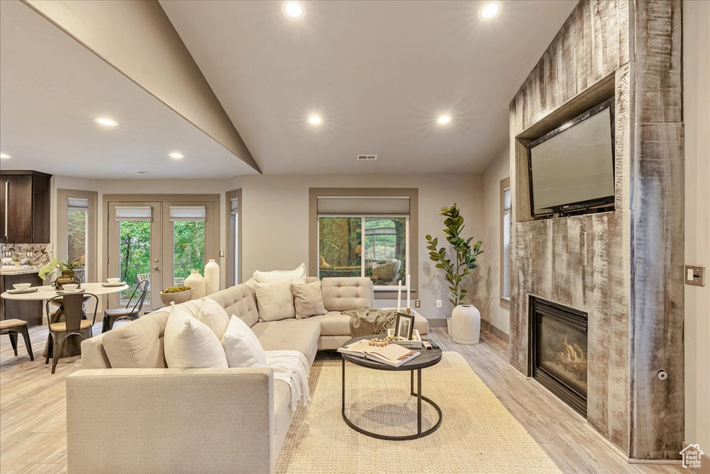 Living room with recessed lighting, a fireplace, plenty of natural light, light wood finished floors, and lofted ceiling