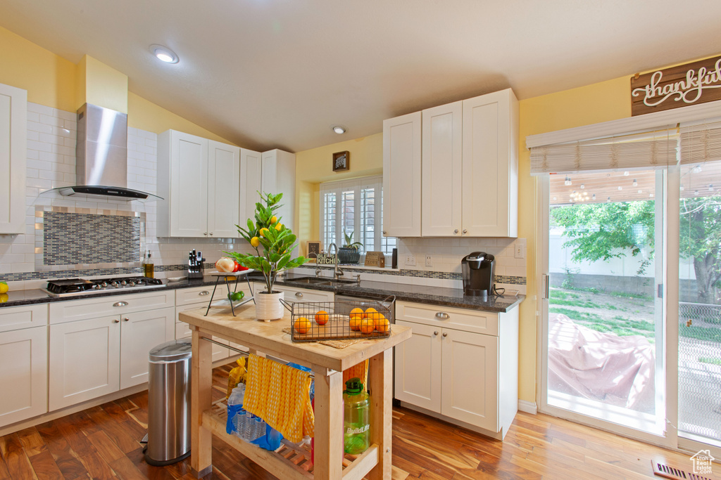 Kitchen with stainless steel gas stovetop, a sink, dark countertops, backsplash, and wood finished floors