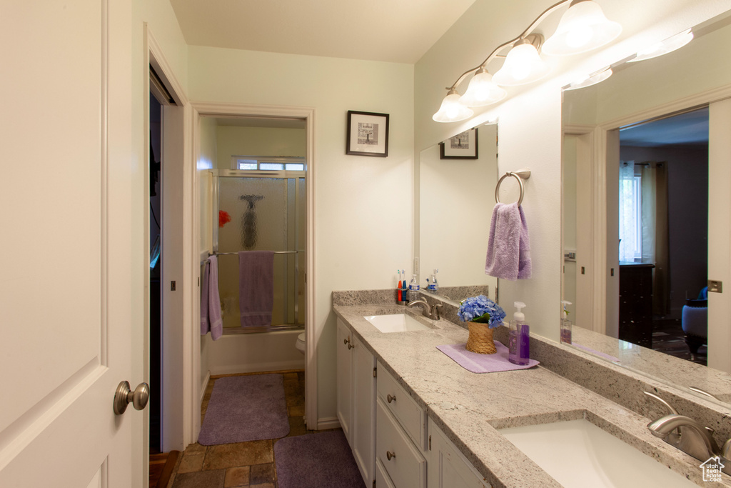 Full bath featuring double vanity, plenty of natural light, stone finish floors, and shower / bath combination with glass door