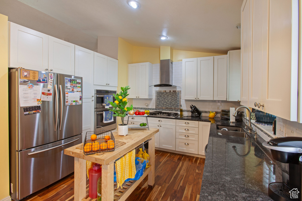 Kitchen featuring stainless steel appliances, a sink, wall chimney exhaust hood, vaulted ceiling, and backsplash
