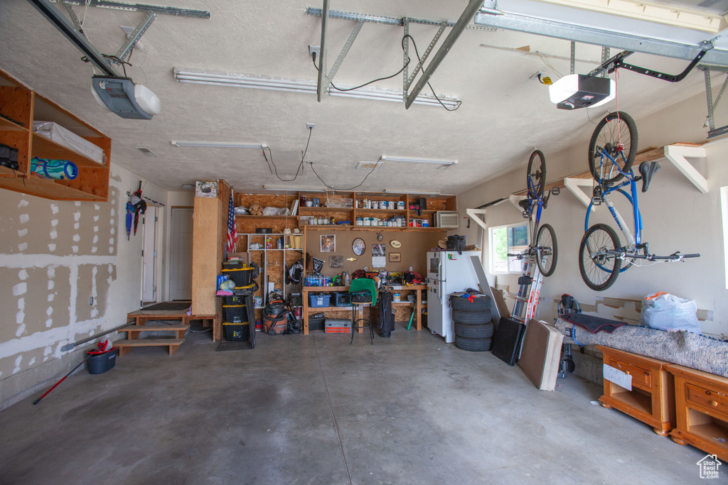 Garage featuring a workshop area, a garage door opener, and freestanding refrigerator