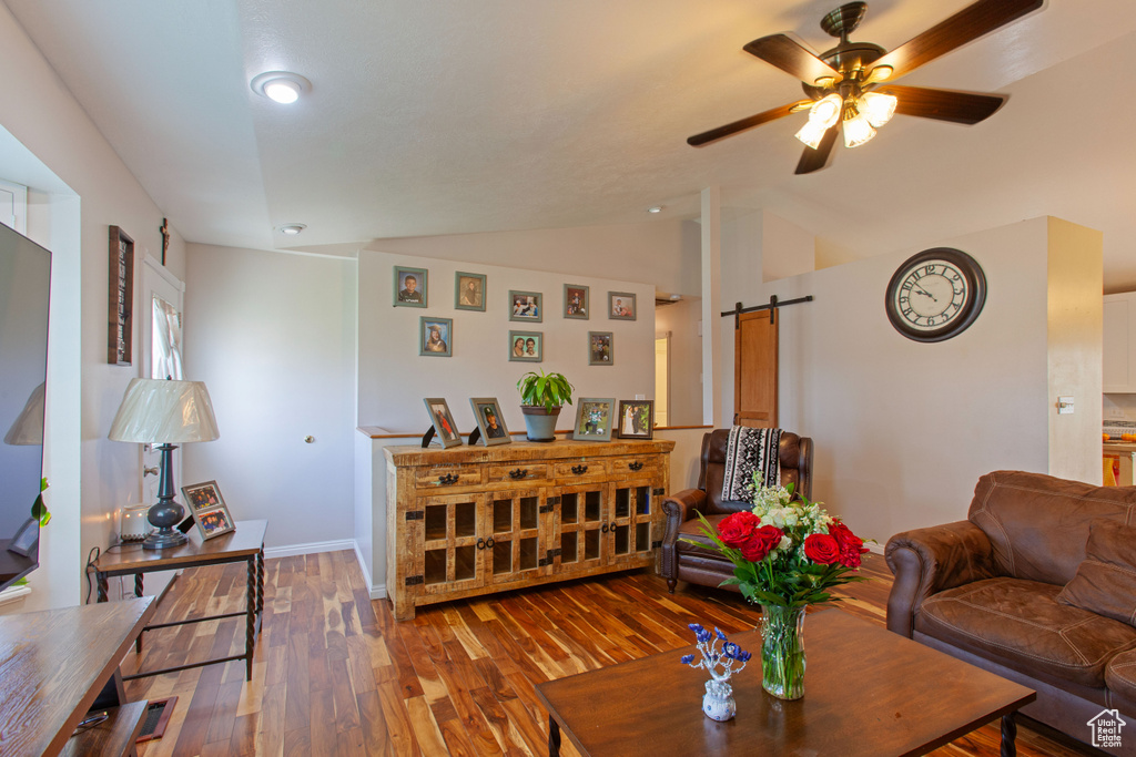 Living area featuring a barn door, lofted ceiling, hardwood / wood-style floors, a ceiling fan, and baseboards