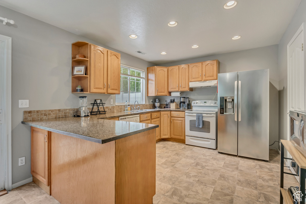 Kitchen featuring white appliances, under cabinet range hood, light brown cabinetry, a peninsula, and a sink