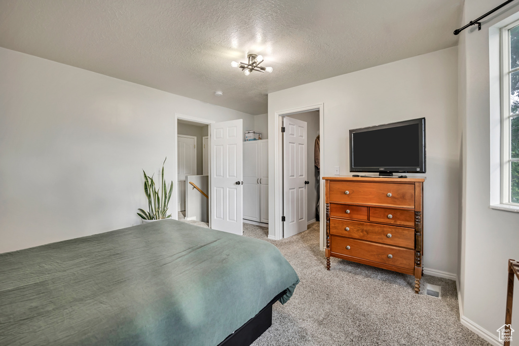Bedroom with a textured ceiling, a chandelier, baseboards, light carpet, and a walk in closet