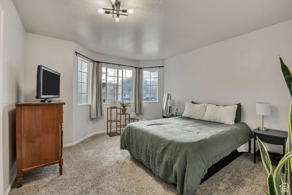 Bedroom with light carpet, baseboards, a textured ceiling, and a chandelier
