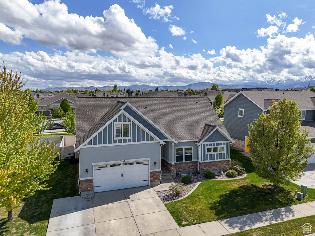 Craftsman-style home with stone siding, concrete driveway, a front yard, a shingled roof, and a residential view