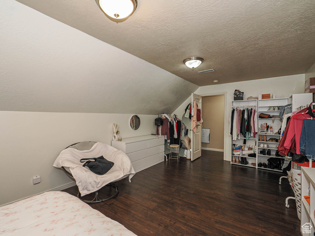 Bedroom featuring wood finished floors, a textured ceiling, vaulted ceiling, and baseboards