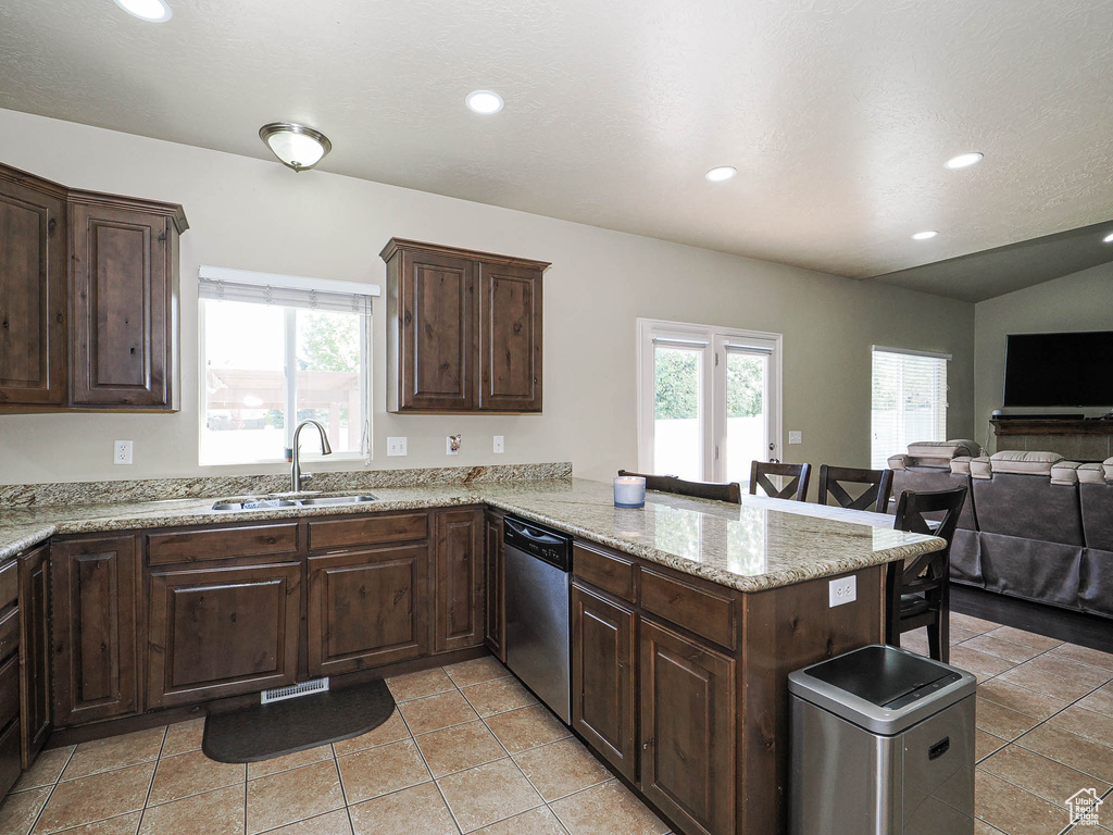 Kitchen featuring stainless steel dishwasher, a sink, a breakfast bar area, open floor plan, and recessed lighting