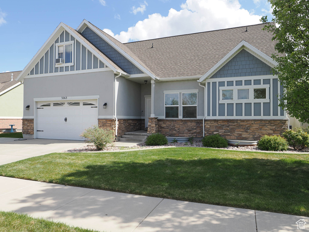 Craftsman-style home featuring stone siding, concrete driveway, stucco siding, a shingled roof, and a front lawn