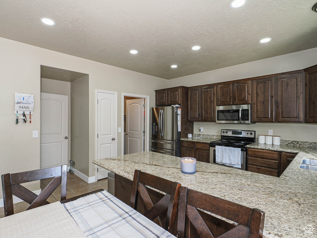 Kitchen with appliances with stainless steel finishes, dark brown cabinetry, baseboards, a kitchen bar, and recessed lighting
