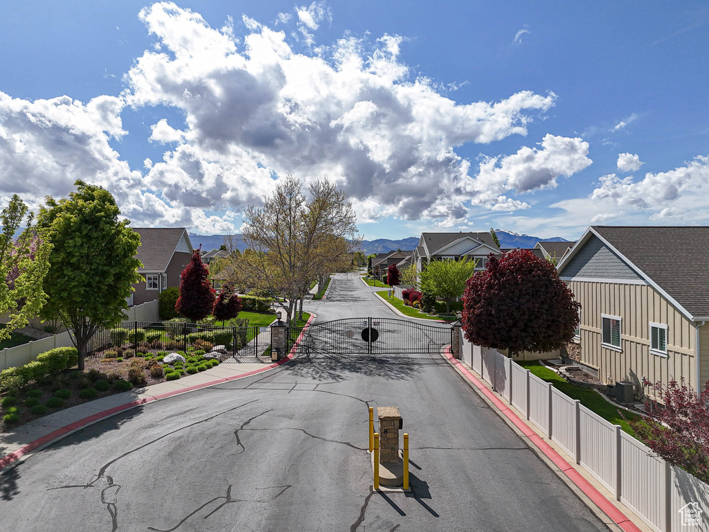 View of asphalt road featuring a residential view, curbs, sidewalks, a gated entry, and a gate