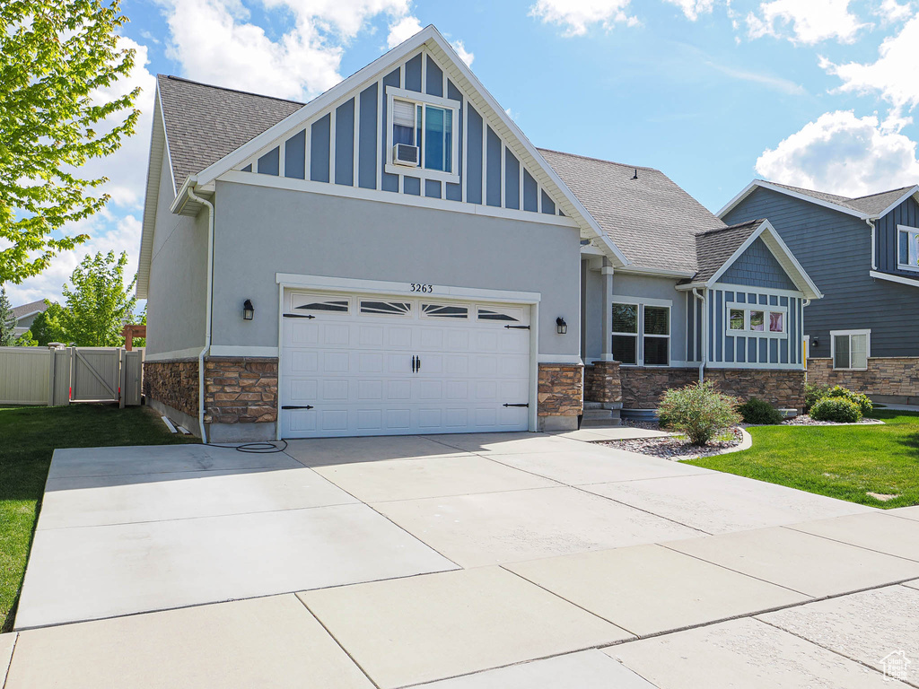 Craftsman-style home featuring stone siding, stucco siding, a shingled roof, concrete driveway, and a gate