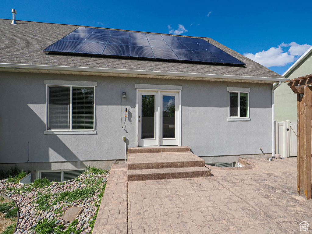 Rear view of house featuring roof with shingles, solar panels, and stucco siding