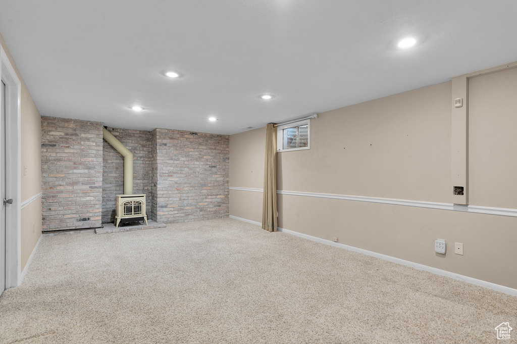 Finished basement with a wood stove, carpet, brick wall, recessed lighting, and baseboards
