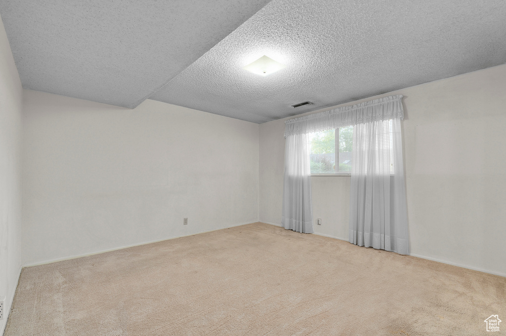Carpeted empty room with a textured ceiling and baseboards