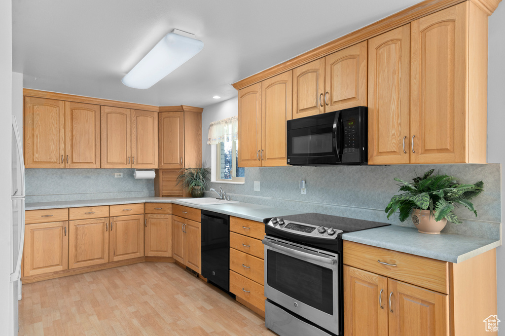 Kitchen featuring black appliances, backsplash, light countertops, and light wood-type flooring