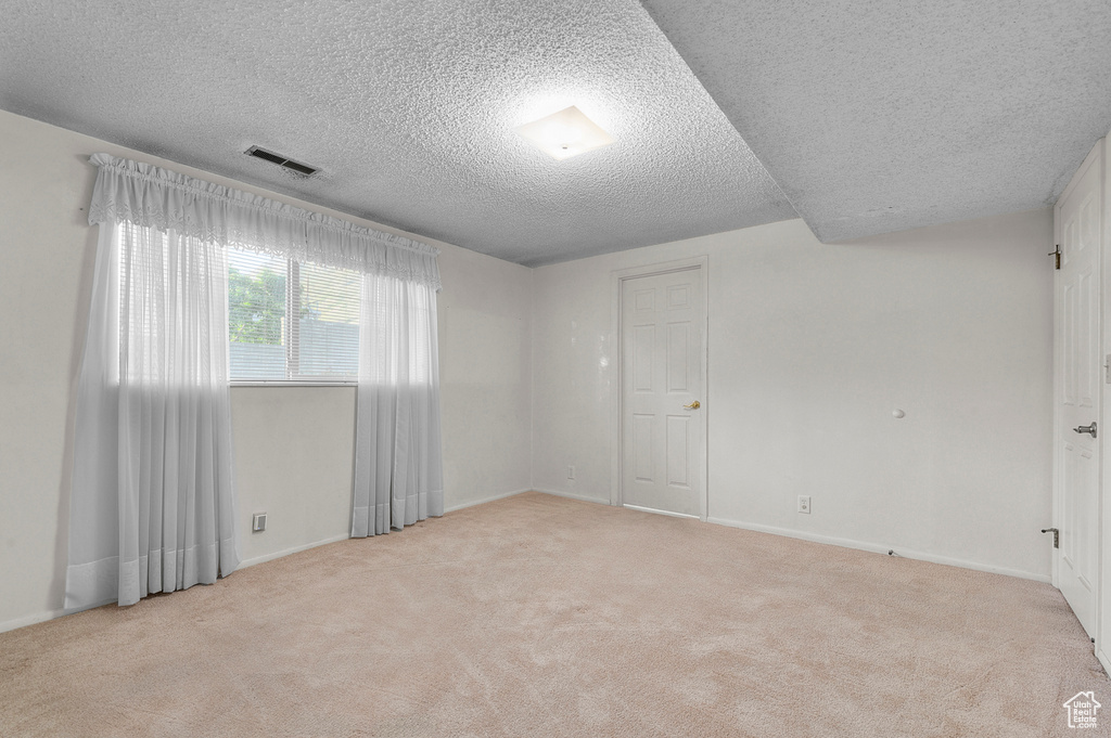 Empty room with a textured ceiling, light colored carpet, and baseboards