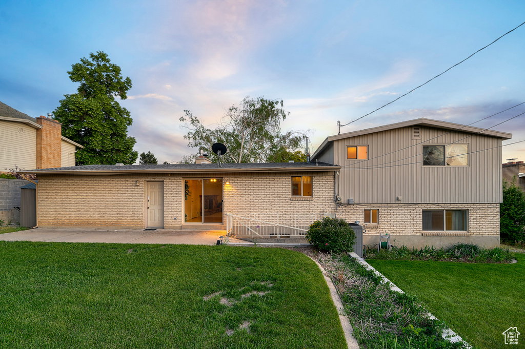Rear view of property featuring brick siding, a patio, and a lawn