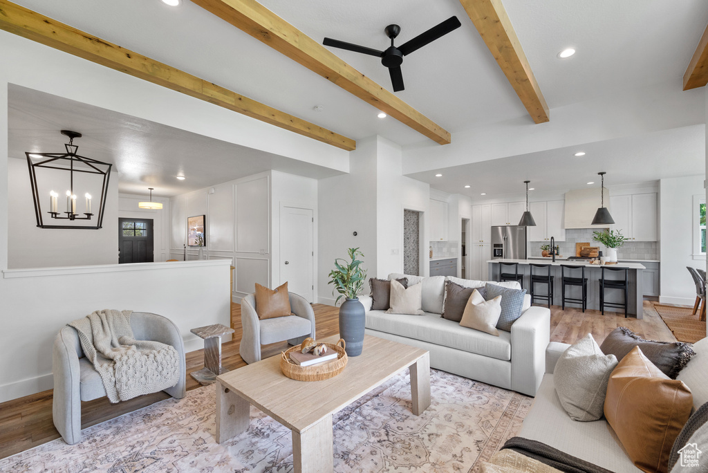 Living area with light wood finished floors, recessed lighting, a chandelier, beam ceiling, and a ceiling fan