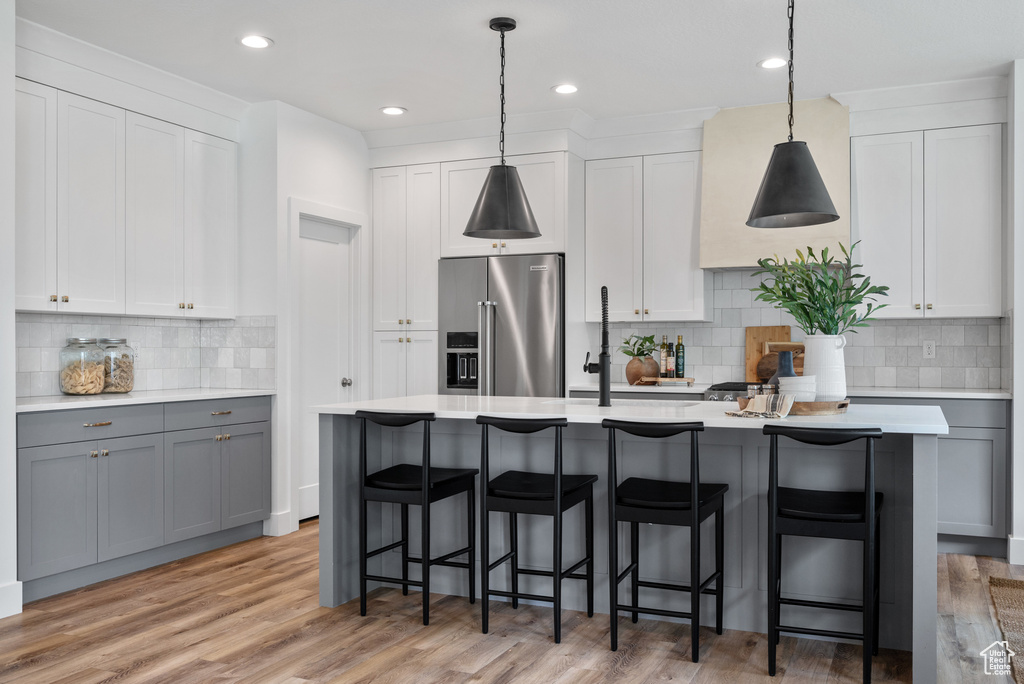 Kitchen featuring high end fridge, a kitchen island with sink, light countertops, backsplash, and decorative light fixtures
