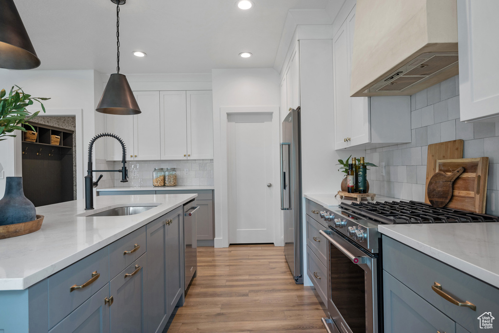 Kitchen with high quality appliances, wall chimney exhaust hood, a sink, white cabinetry, and recessed lighting