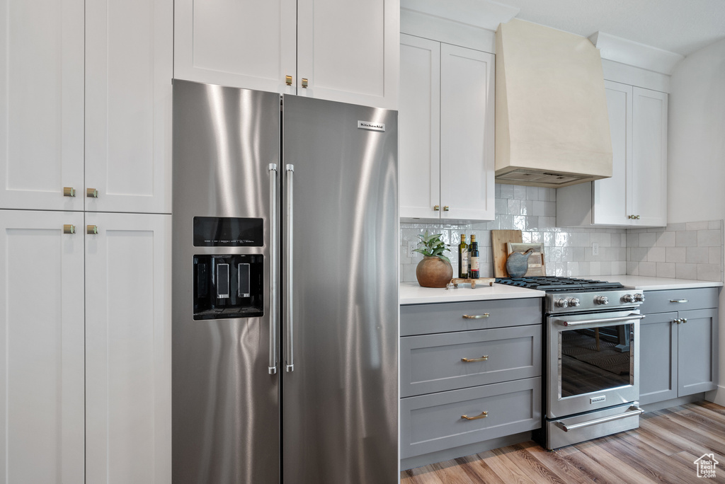 Kitchen with premium appliances, premium range hood, gray cabinetry, light countertops, and tasteful backsplash